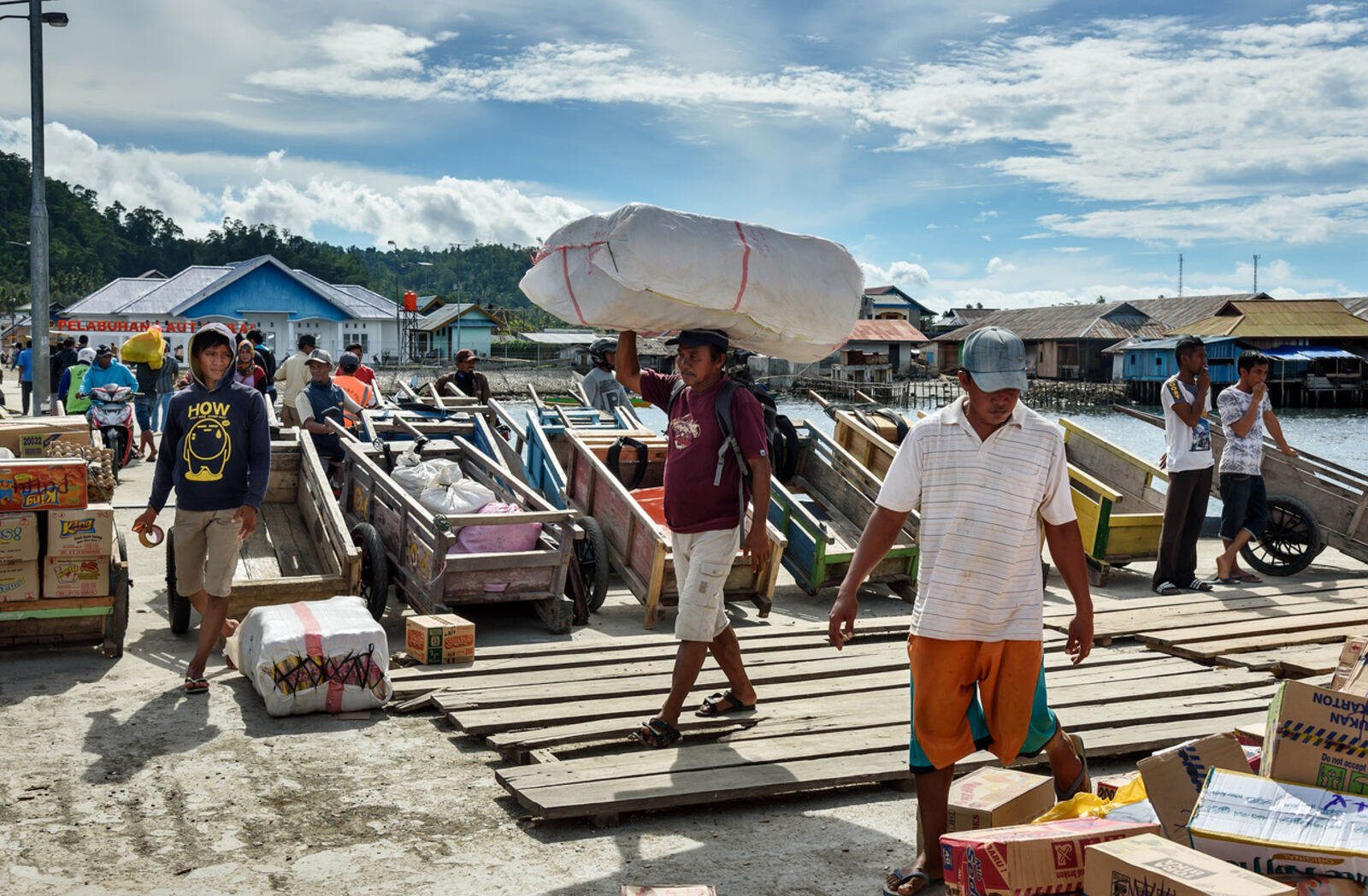 Workers unloading goods from wooden boats at a coastal port — the human reality of regulated supply chains